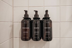 Drei Flaschen 'Home Hotel'-Produkte: Conditioner, Shampoo und Duschgel, jede mit Inhaltsangabe und Vegan-Zertifizierung versehen.