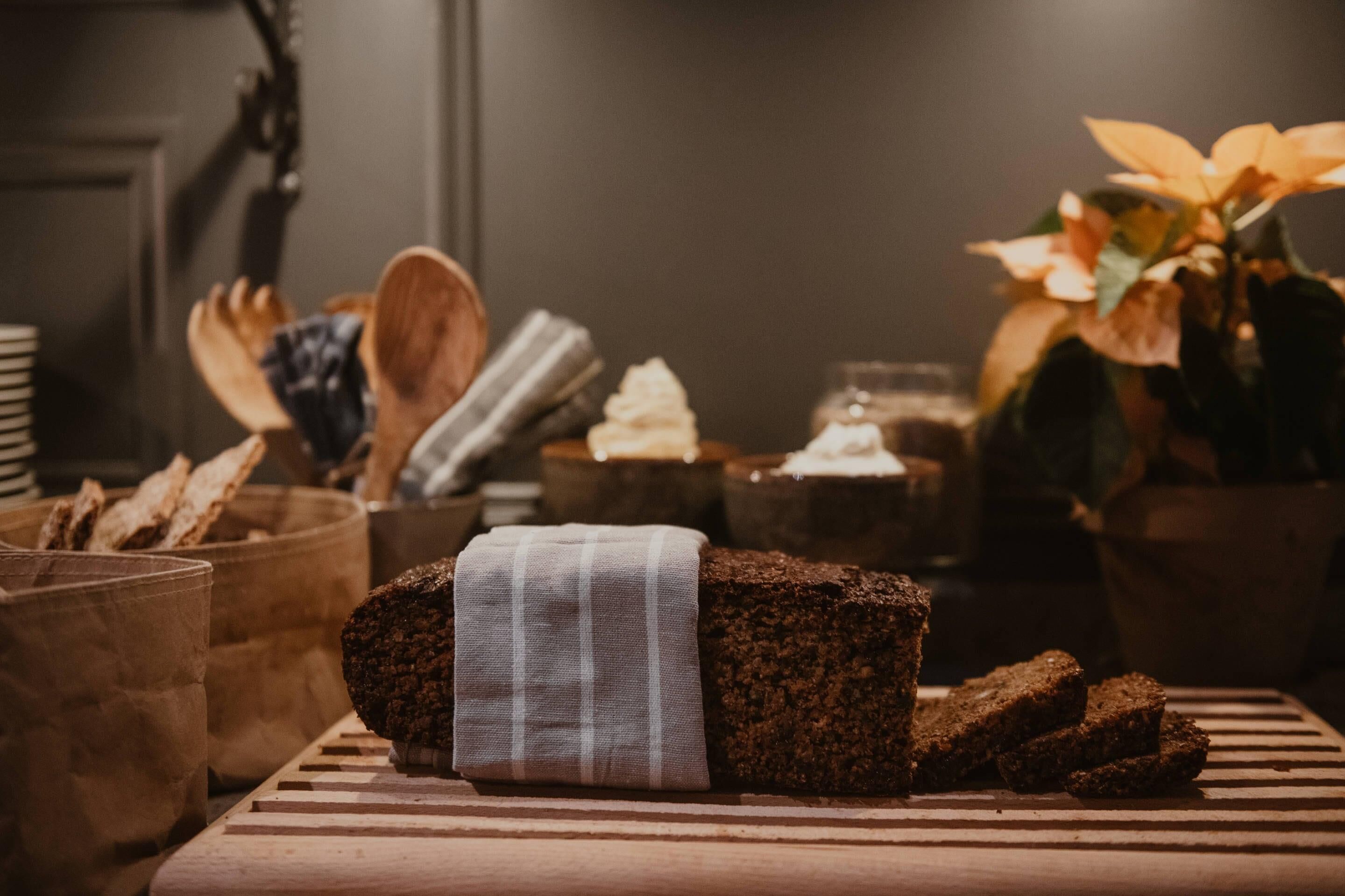 A loaf of bread wrapped in cloth on a wooden board, surrounded by bread baskets and a potted plant.