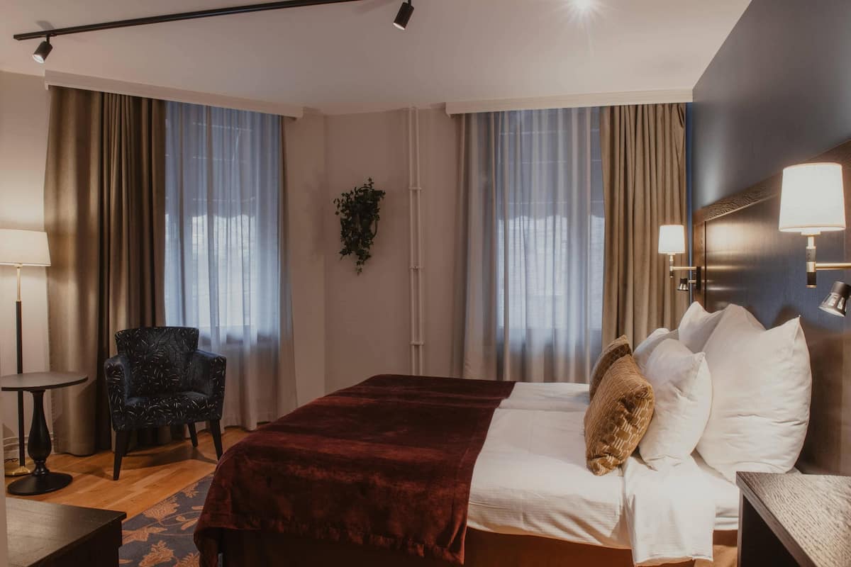 Une chambre d’hôtel avec un grand lit, une chaise, une petite table et une lampe fixée au mur.
