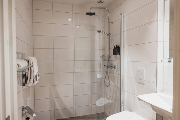 A modern bathroom with a glass-enclosed shower, a white sink, and neatly folded towels on a shelf.