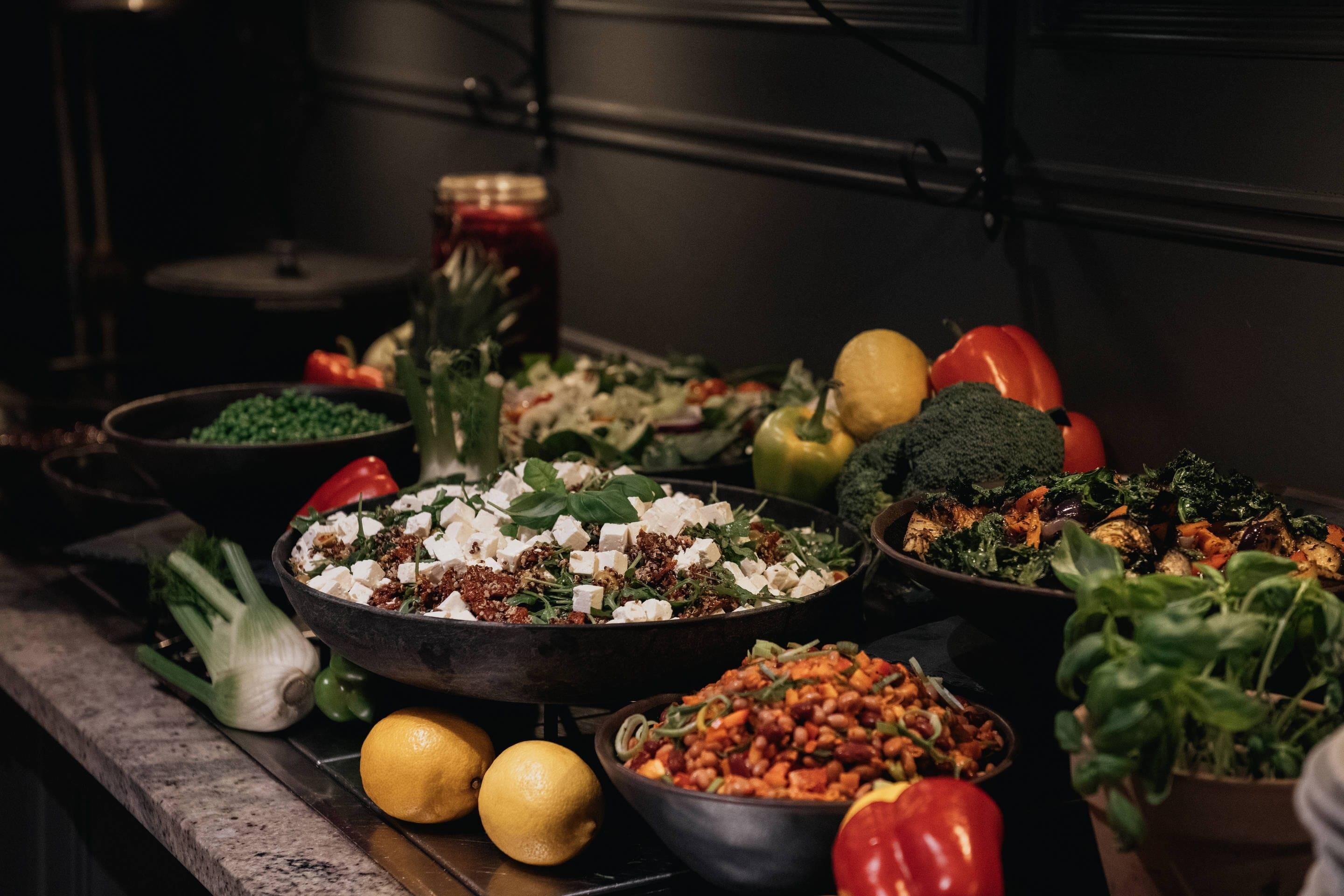 A variety of dishes and fresh vegetables on a table in a kitchen setting.