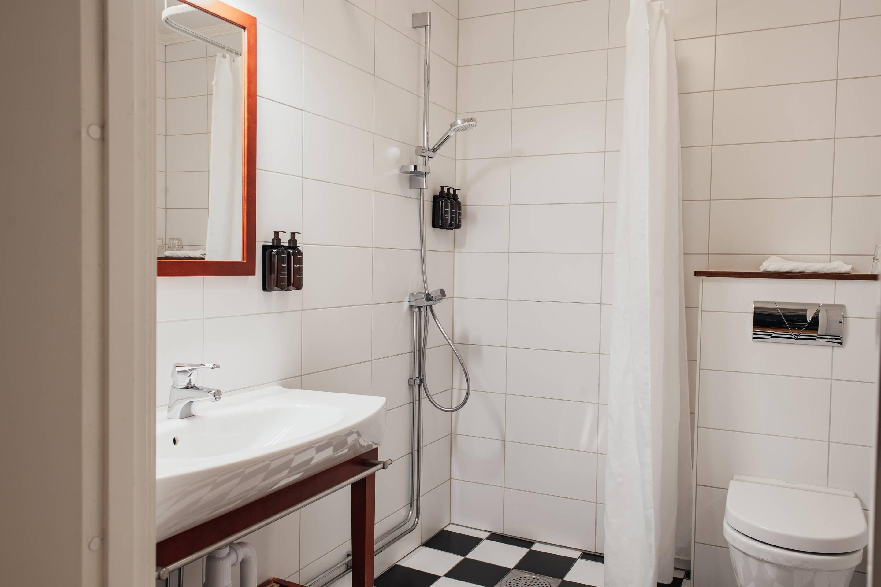 Un baño pequeño y limpio con lavamanos blanco, espejo, ducha e inodoro.