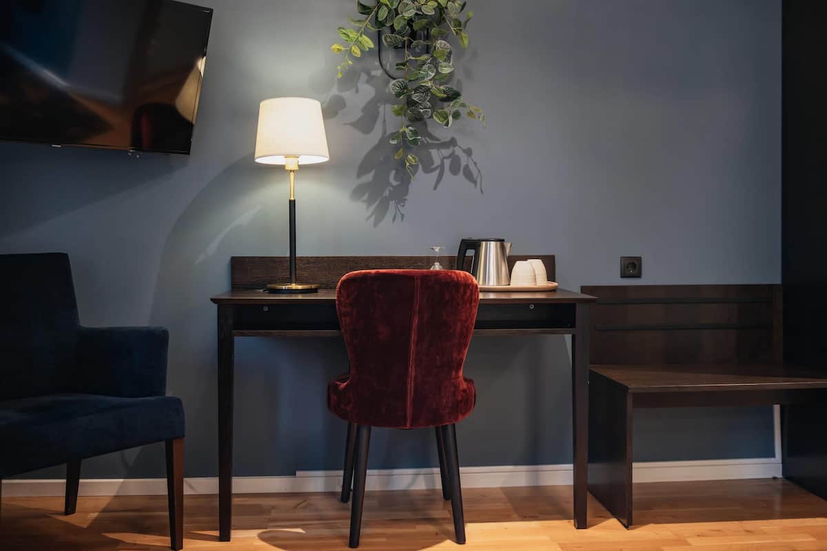 Une pièce moderne avec un mur bleu foncé, un bureau en bois, un fauteuil en velours rouge, une lampe et une plante.
