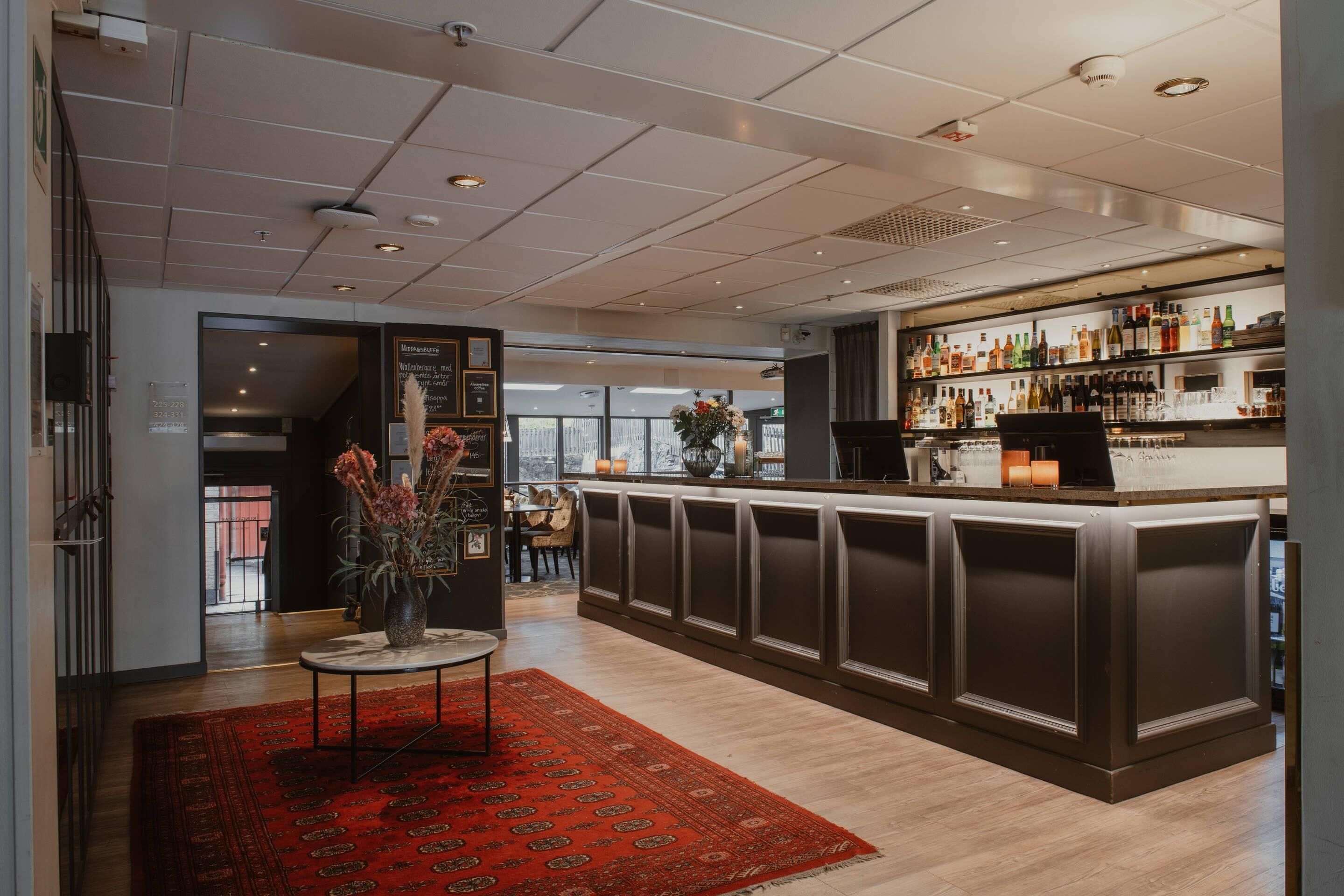 A bar area with a long counter, a red patterned rug, and a wall of liquor bottles.