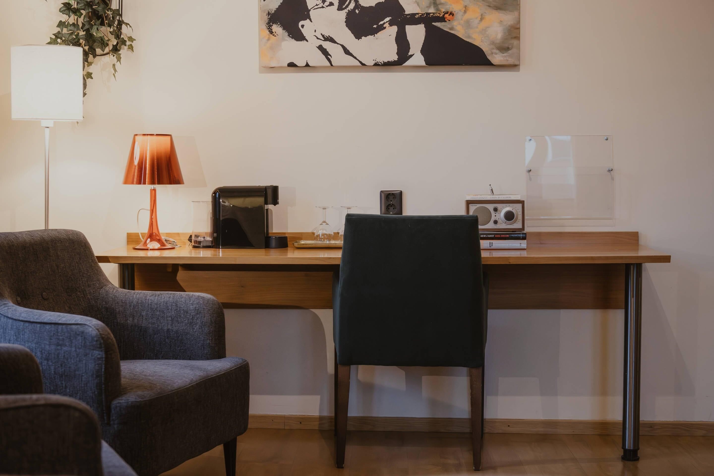 Una habitación moderna con un escritorio de madera, dos sillas, una lámpara, un radio y una obra de arte enmarcada en la pared.