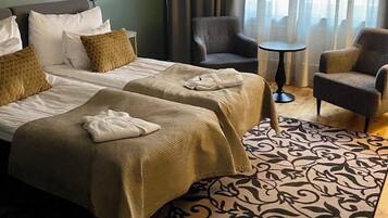 A hotel room with two beds, a chair, a small table, and a patterned rug.
