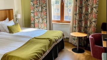 Ett hotellrum med en säng, ett litet runt bord, en stol och gardiner med ett blommönster.