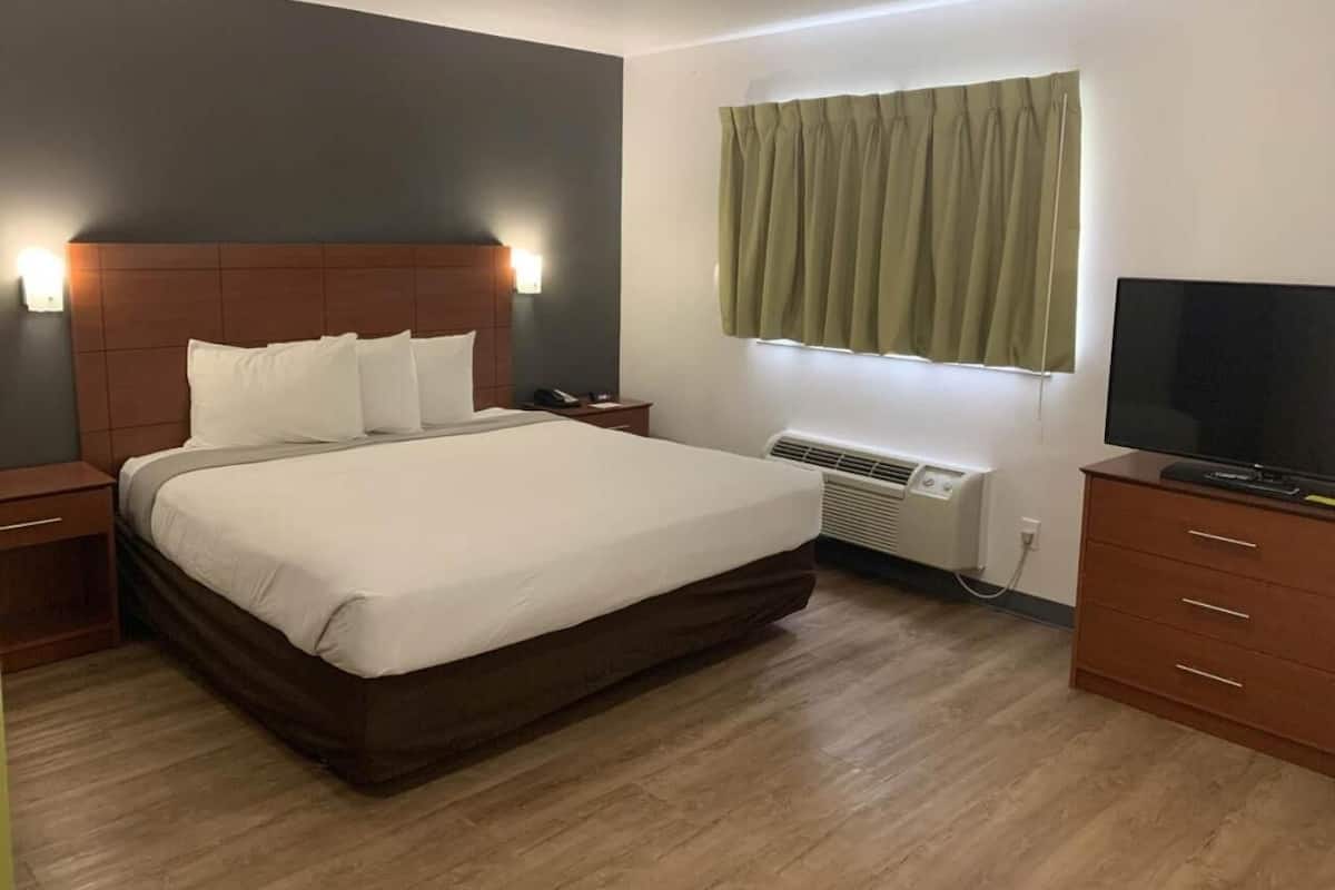 A hotel room with a large bed, bedside tables, a TV, and a window with curtains.