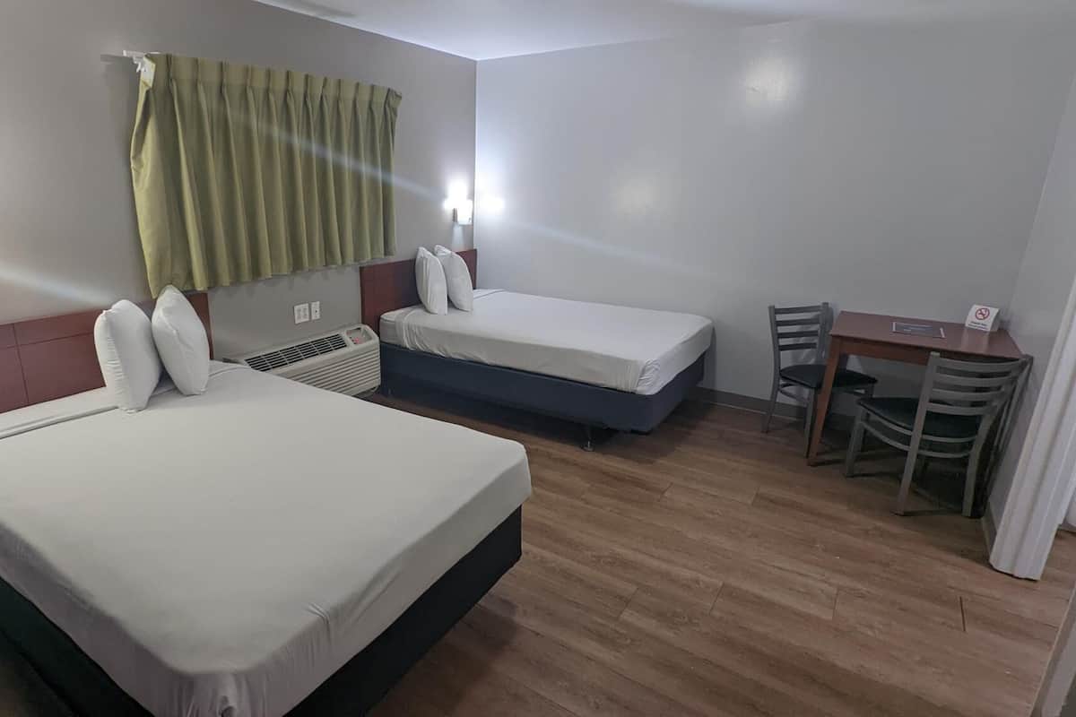A hotel room with two single beds, a desk, and a chair.