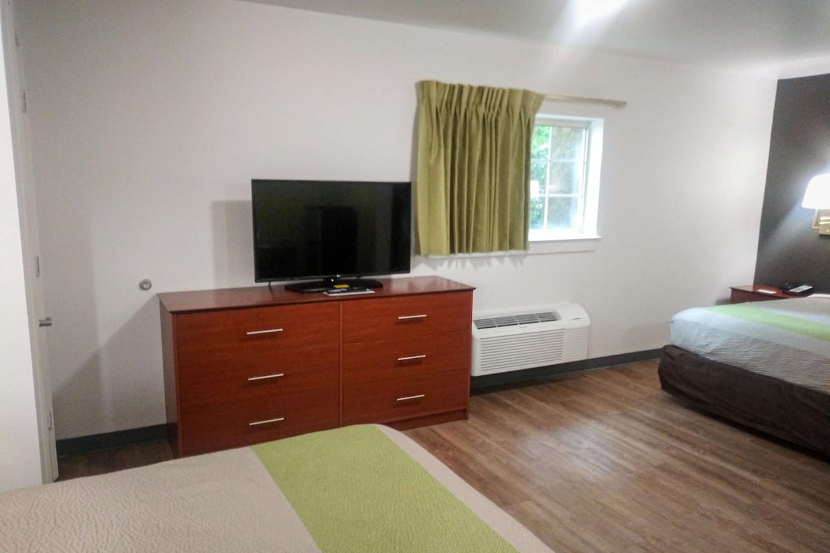 A bedroom with a wooden dresser, a television, a bed, and a window with curtains.