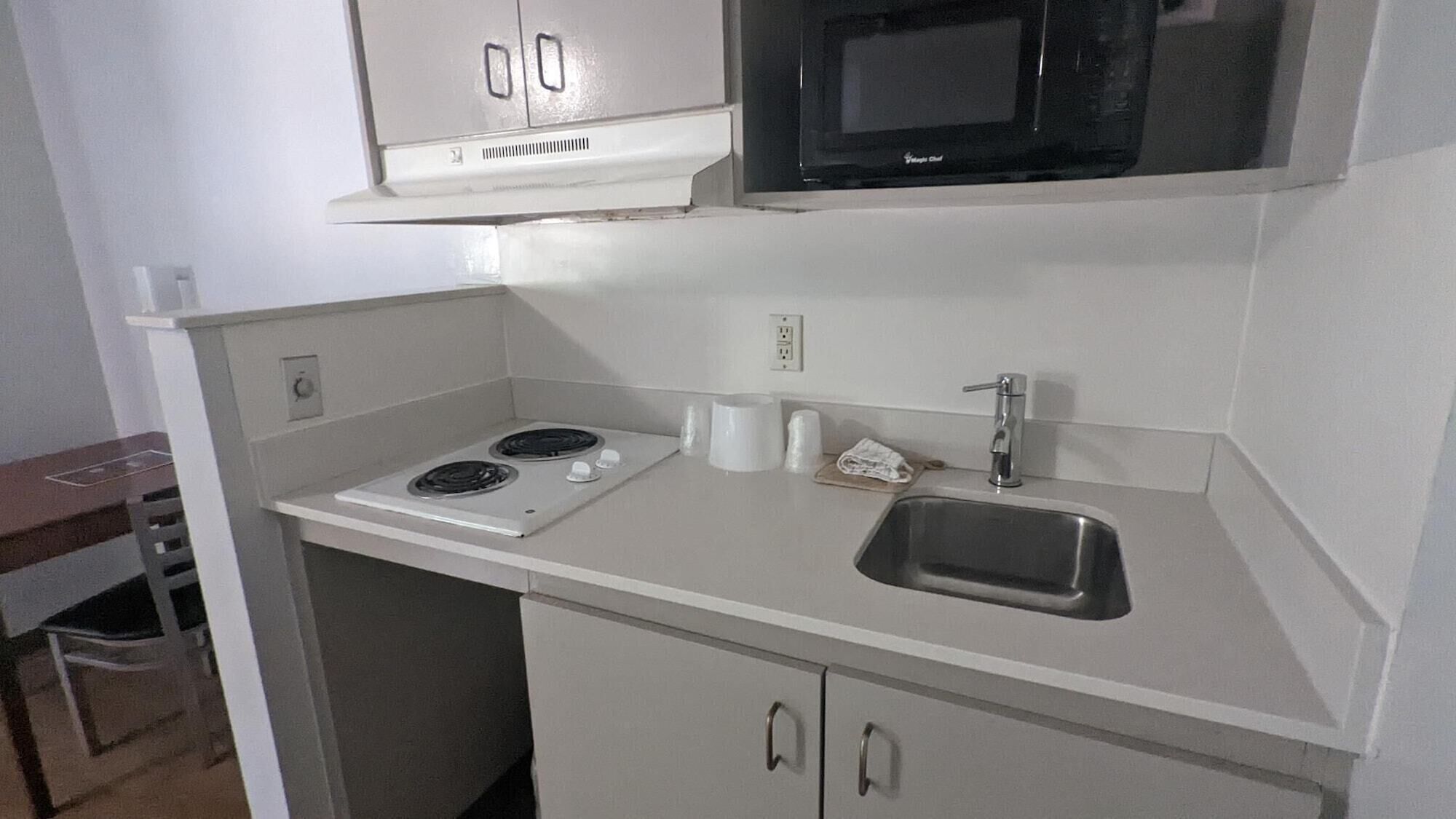 Una cocina compacta con armarios blancos, estufa, microondas y fregadero.