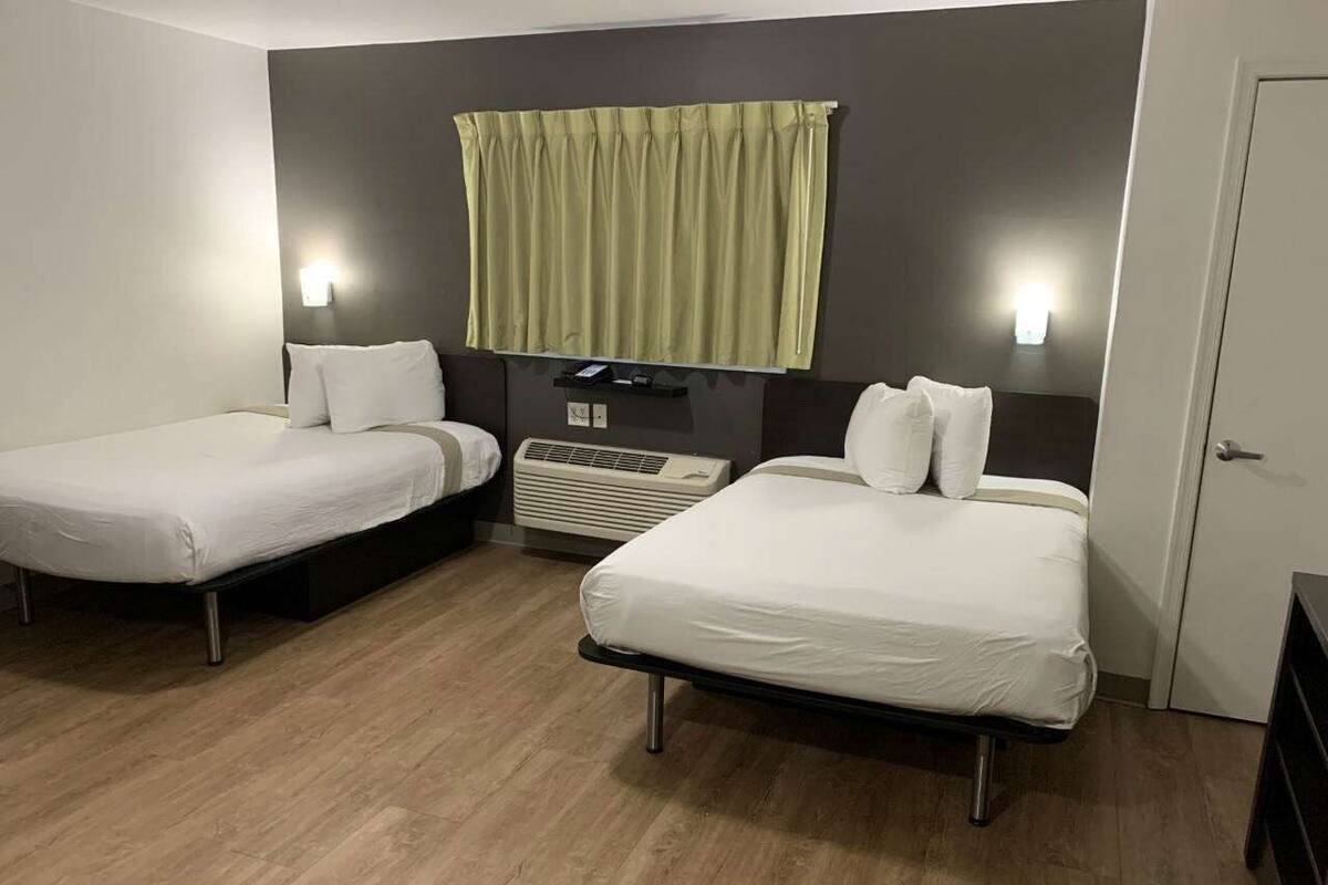 A hotel room with two single beds, a heater, and a wall-mounted light fixture.