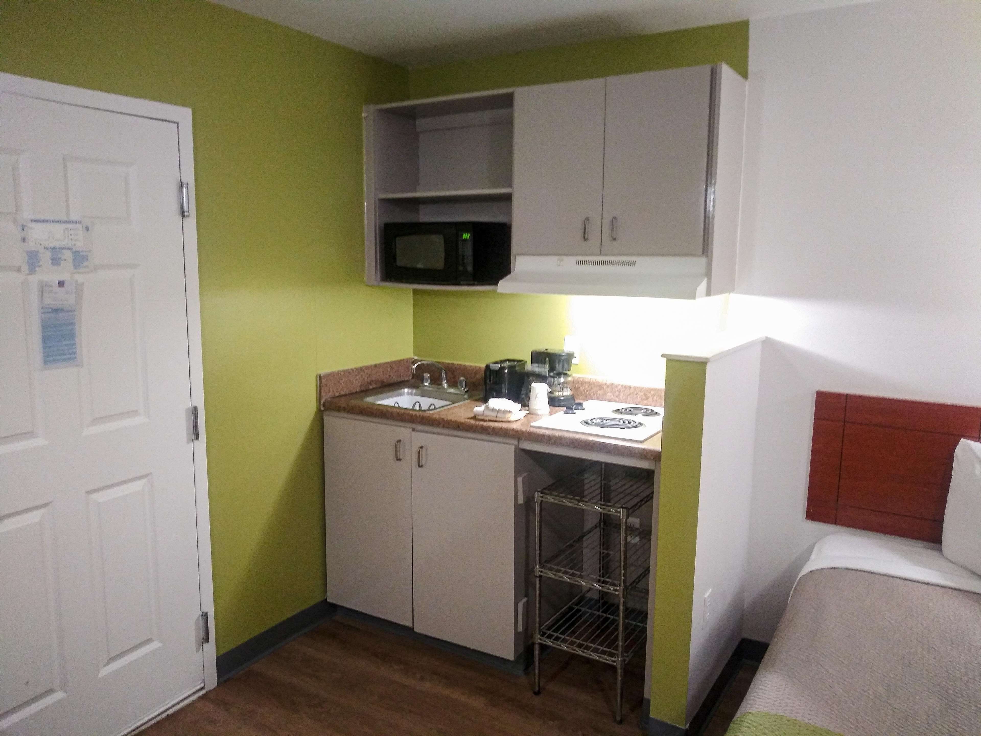 A compact kitchen with a microwave, sink, and stove, adjacent to a bed with a headboard.