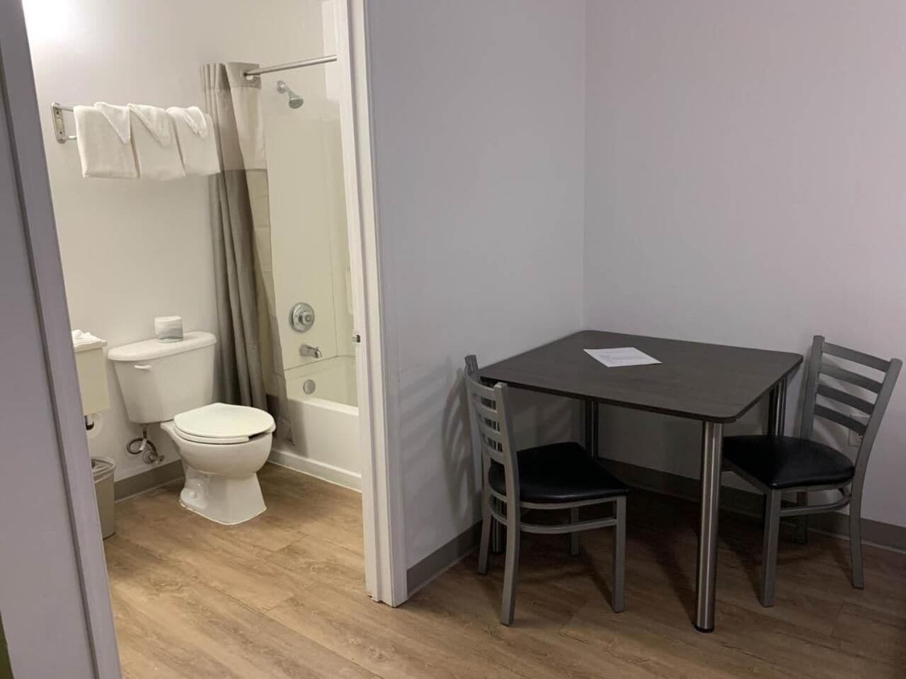 A small bathroom with a toilet, shower, and a table with two chairs.