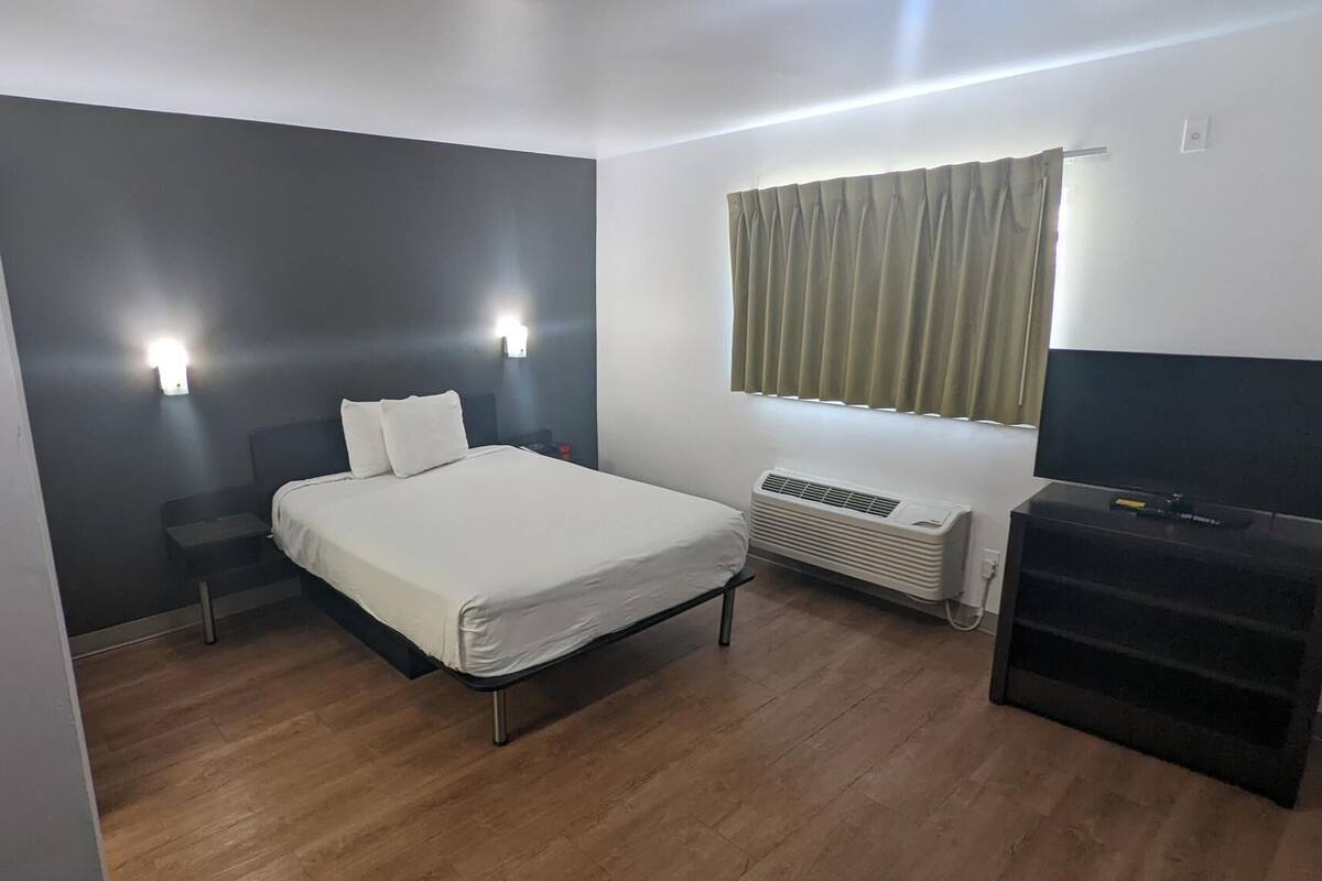 A bedroom with a bed, bedside lamps, a heater, a TV, and a window with curtains.