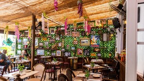 En restaurang med trämöbler, hängande växter och inramade tavlor på väggarna.