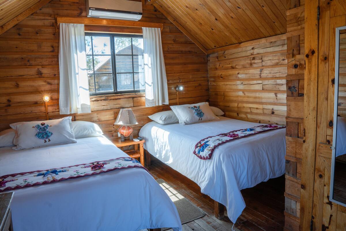 Une cabine avec deux lits en bois, une fenêtre avec des rideaux, une lampe et une petite table.