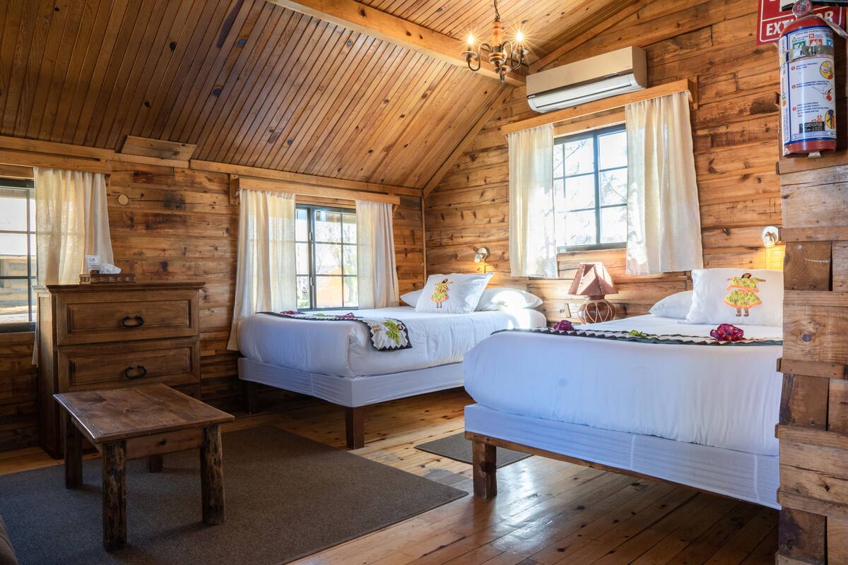 Une cabine avec deux lits, un plancher en bois, un lustre et un extincteur.