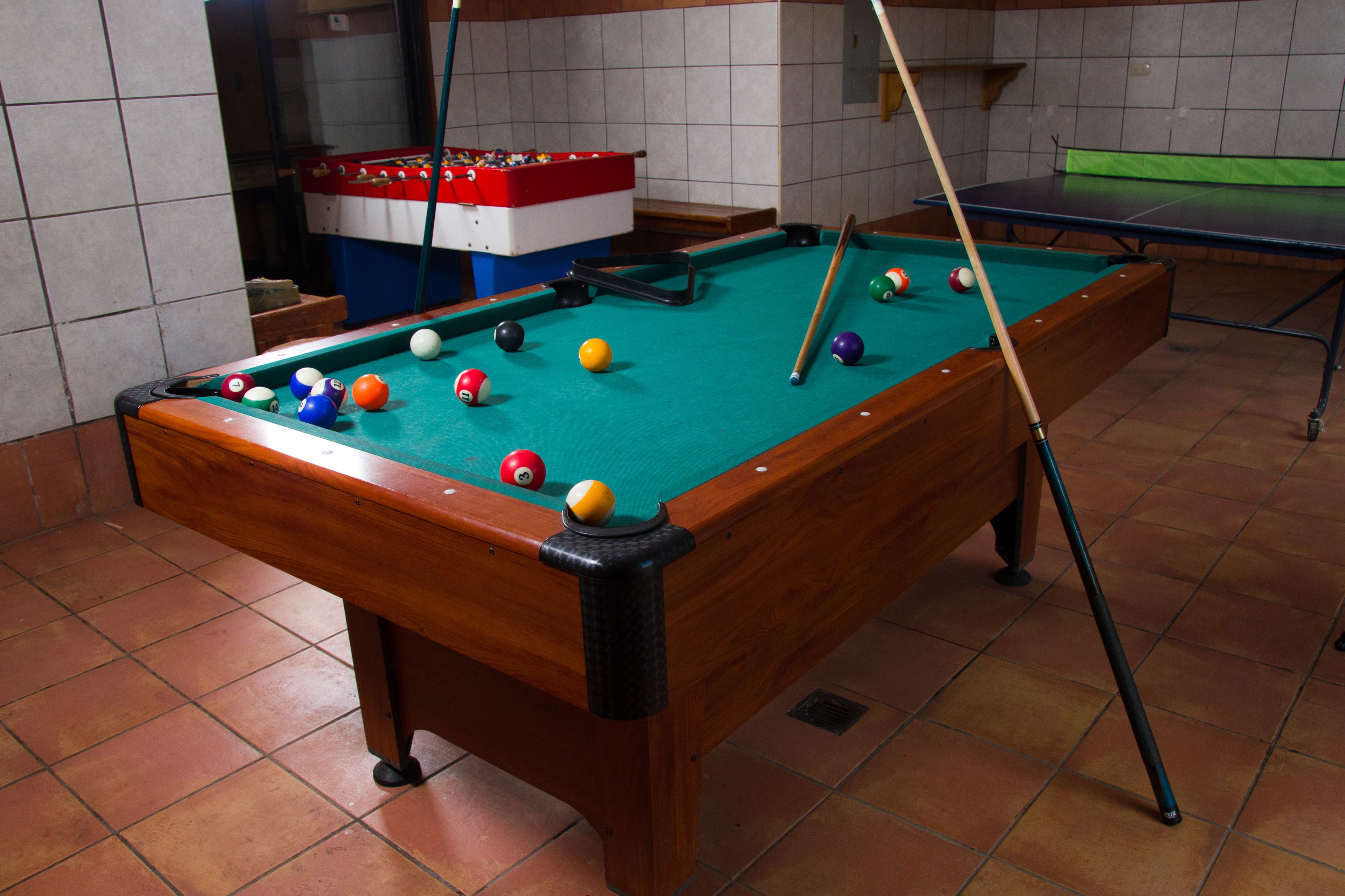 A pool table with balls, a foosball table, and a billiard cue.