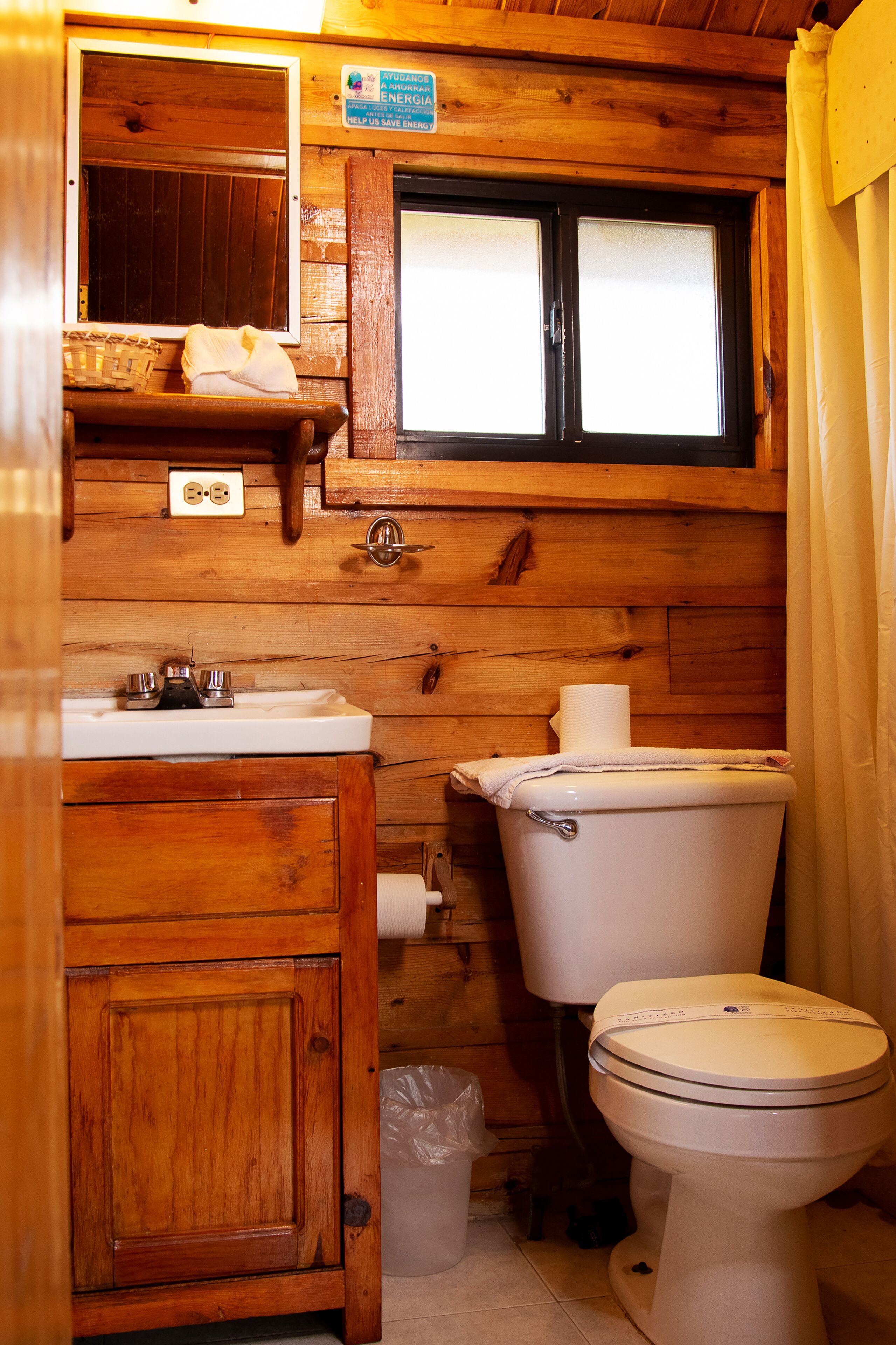 A wooden cabin-style bathroom with a wooden sink, a toilet, and a window with blinds.