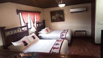 Habitación con dos camas, cabeceros de madera, suelo de madera, un cuadro en la pared y una ventana con cortinas.