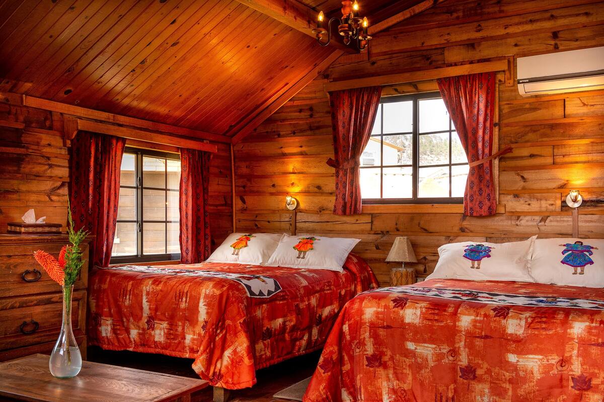 Une chambre de style cabane avec deux lits, des murs en bois, un plafond en bois, une fenêtre avec des rideaux et un appareil de climatisation.