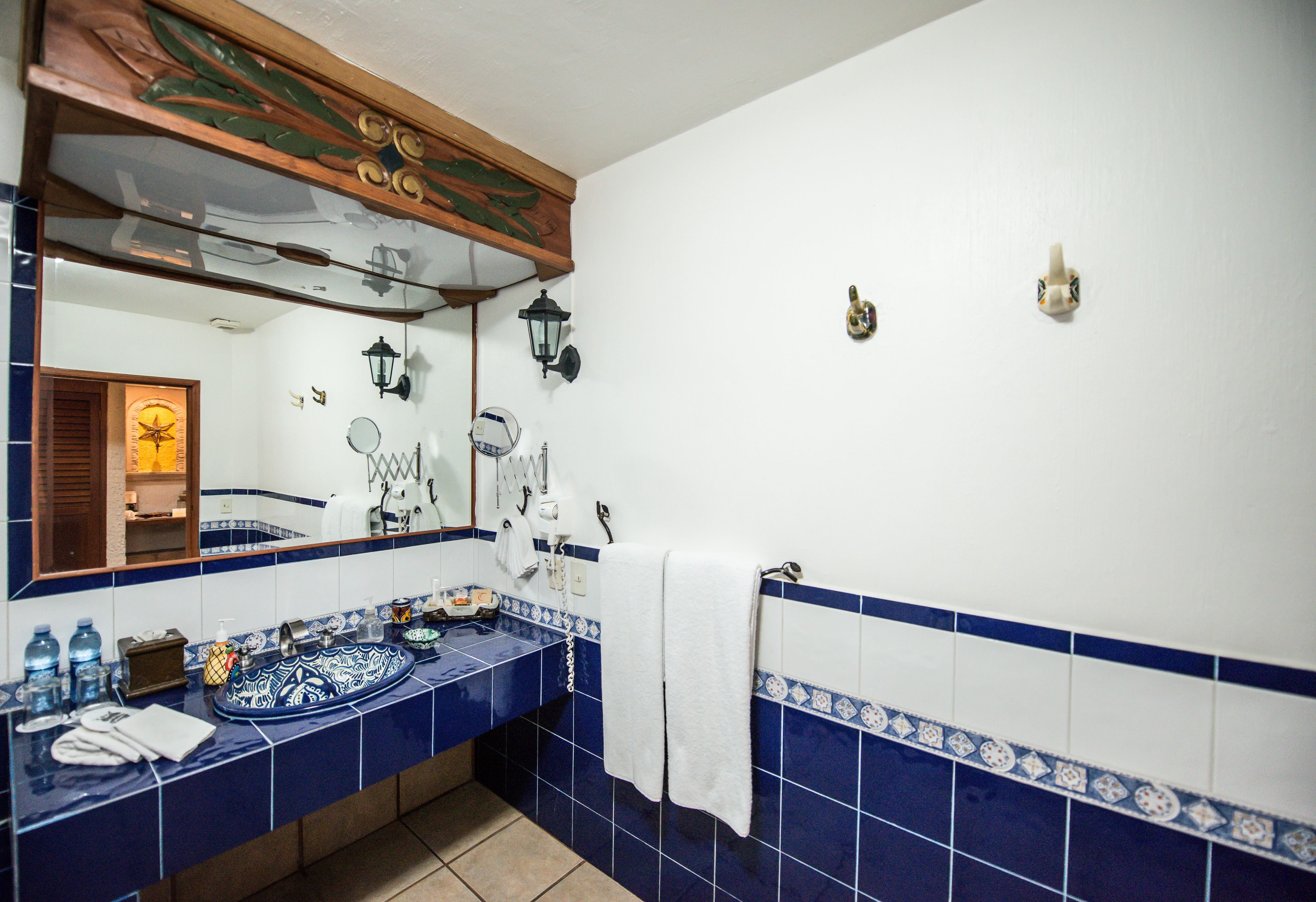 Ein Badezimmer mit blau-weißen Fliesen an der Rückwand, einem Holzlagerflanschrank, einem Spiegel und einem Handtuchhalter.