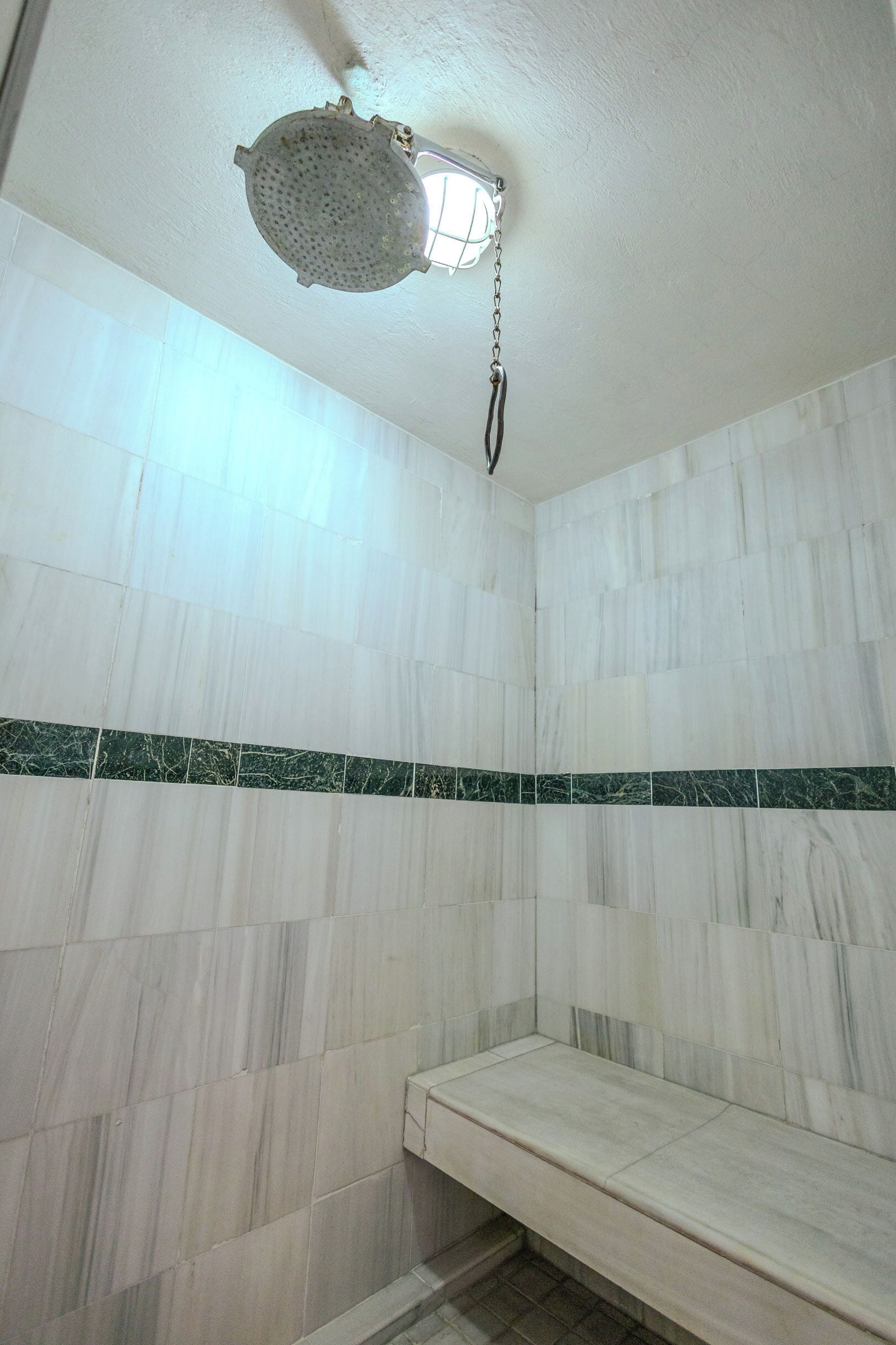 Un baño con azulejos de mármol blanco, un borde de mármol verde y un cabezal de ducha.