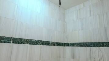 Un baño con azulejos de mármol blanco, un borde de mármol verde y un cabezal de ducha.