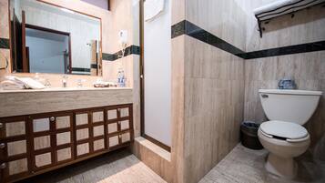 A bathroom with a marble vanity, a large mirror, a toilet, and a trash bin.