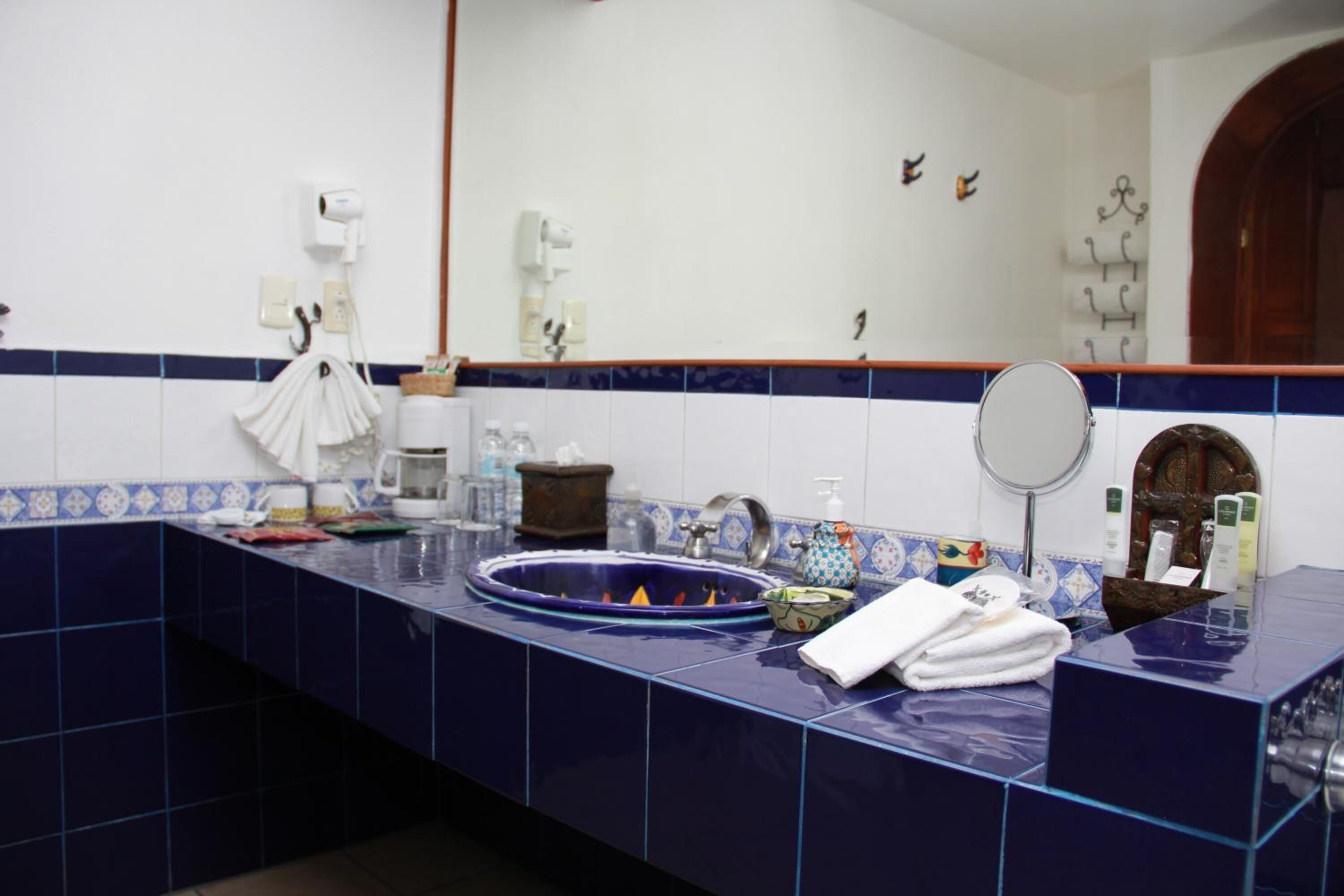 Un baño con mostrador azulado de azulejos, un lavamanos, un espejo y varios artículos de tocador.