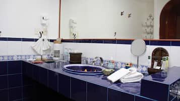 Un baño con mostrador azulado de azulejos, un lavamanos, un espejo y varios artículos de tocador.