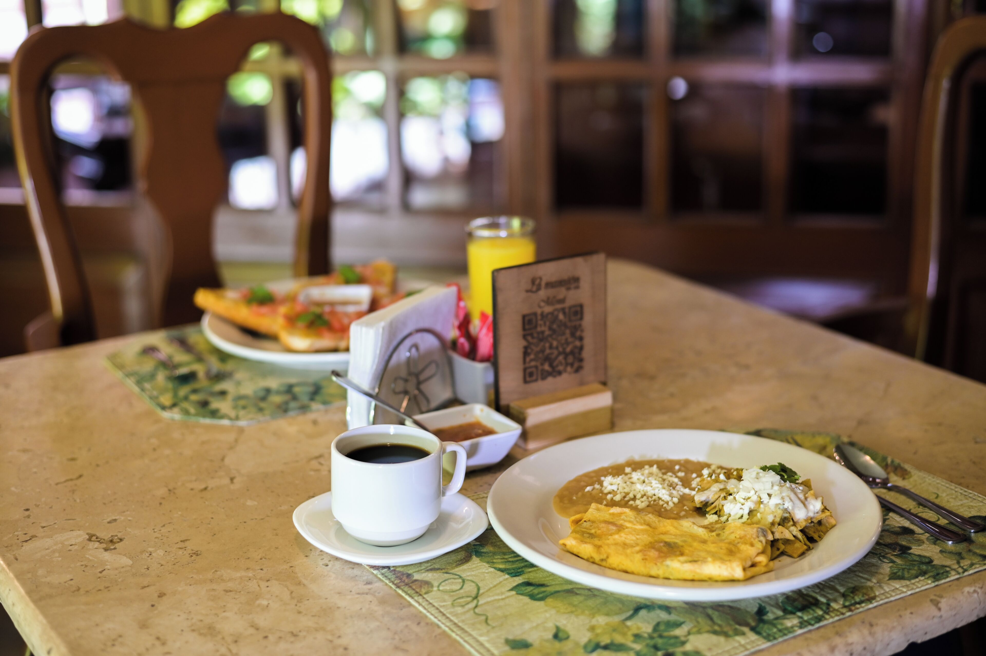 A dining table with a plate of enchiladas, a cup of coffee, and a QR code menu.