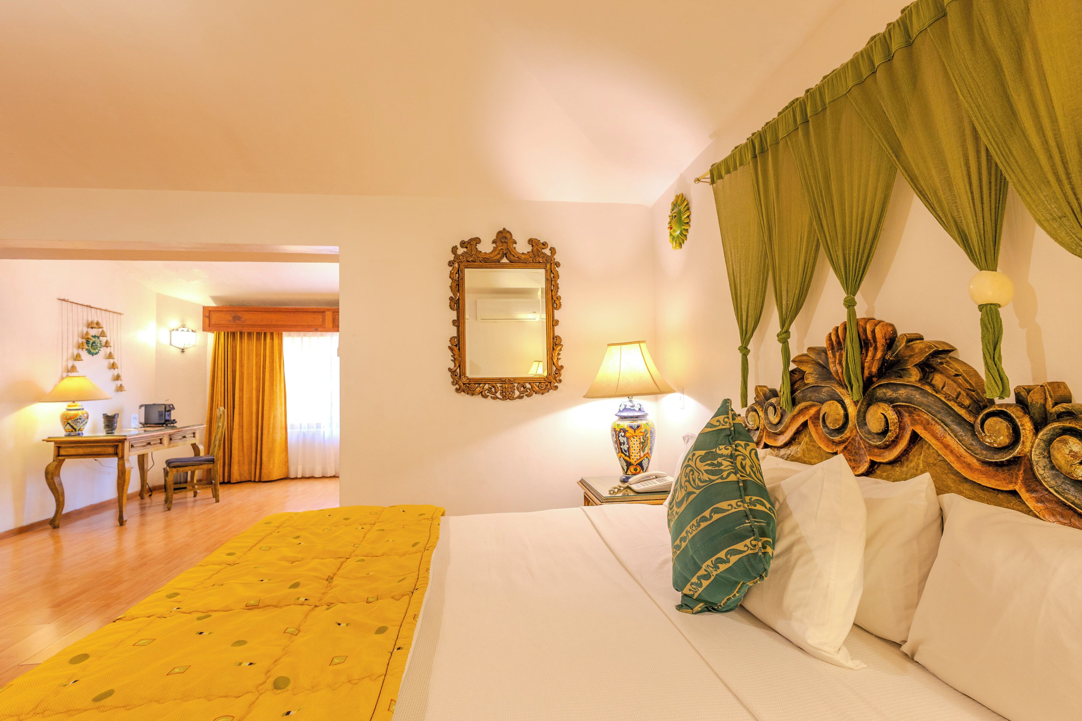 A hotel room with a bed, a desk, a chair, a lamp, and a mirror.