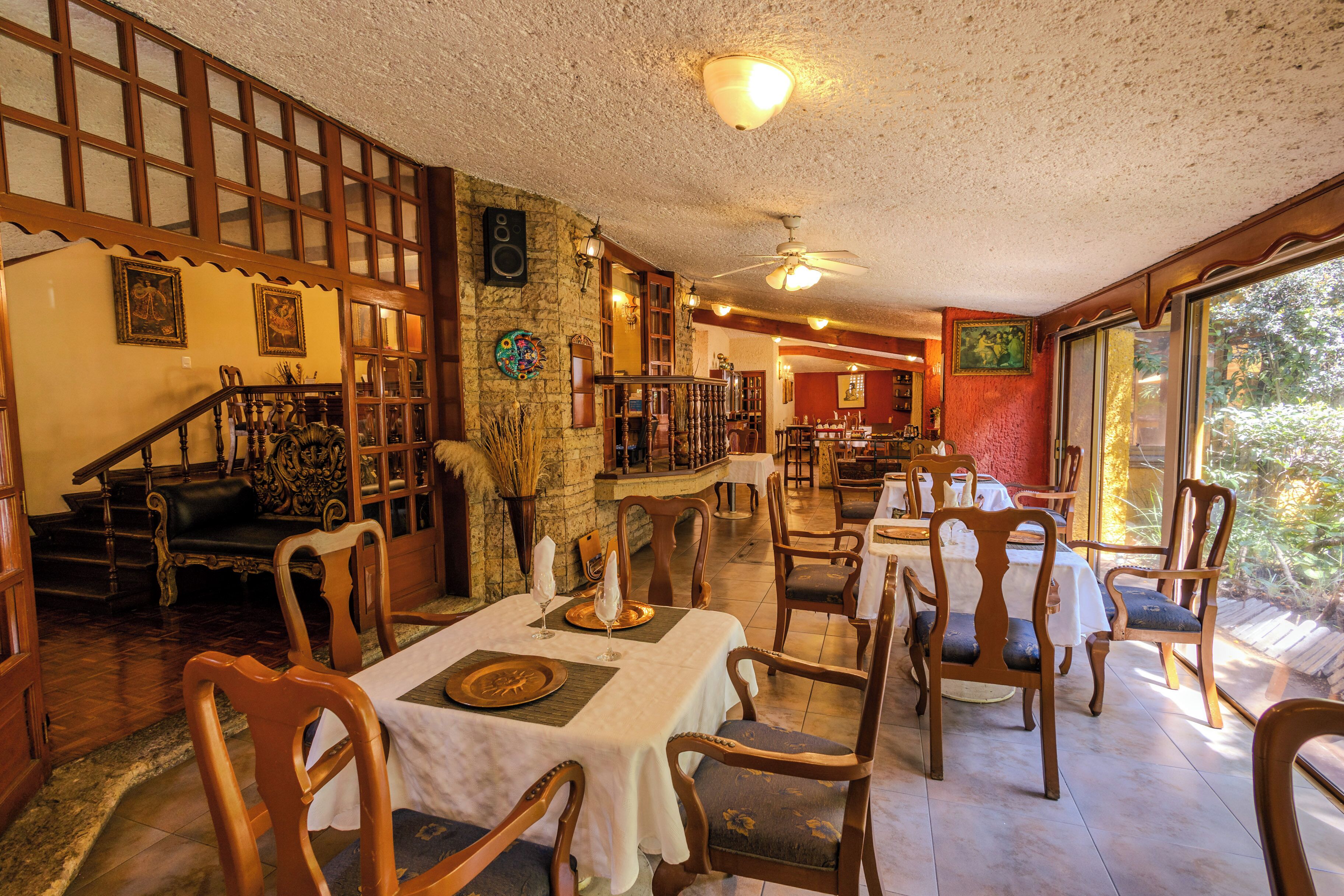 Zona pranzo con sedie e tavoli di legno, una scala e vista panoramica attraverso ampie finestre.