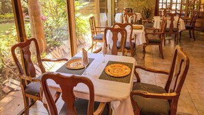 A restaurant with wooden chairs and tables, large windows, and a stone wall. - La Mansiรณn del Sol (Zapopan)