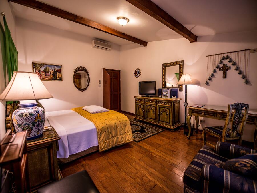 Una habitación con cama, escritorio, silla, televisión y espejo.