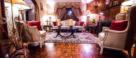A classic room with a wooden parquet floor, a central coffee table, and two armchairs with red cushions.