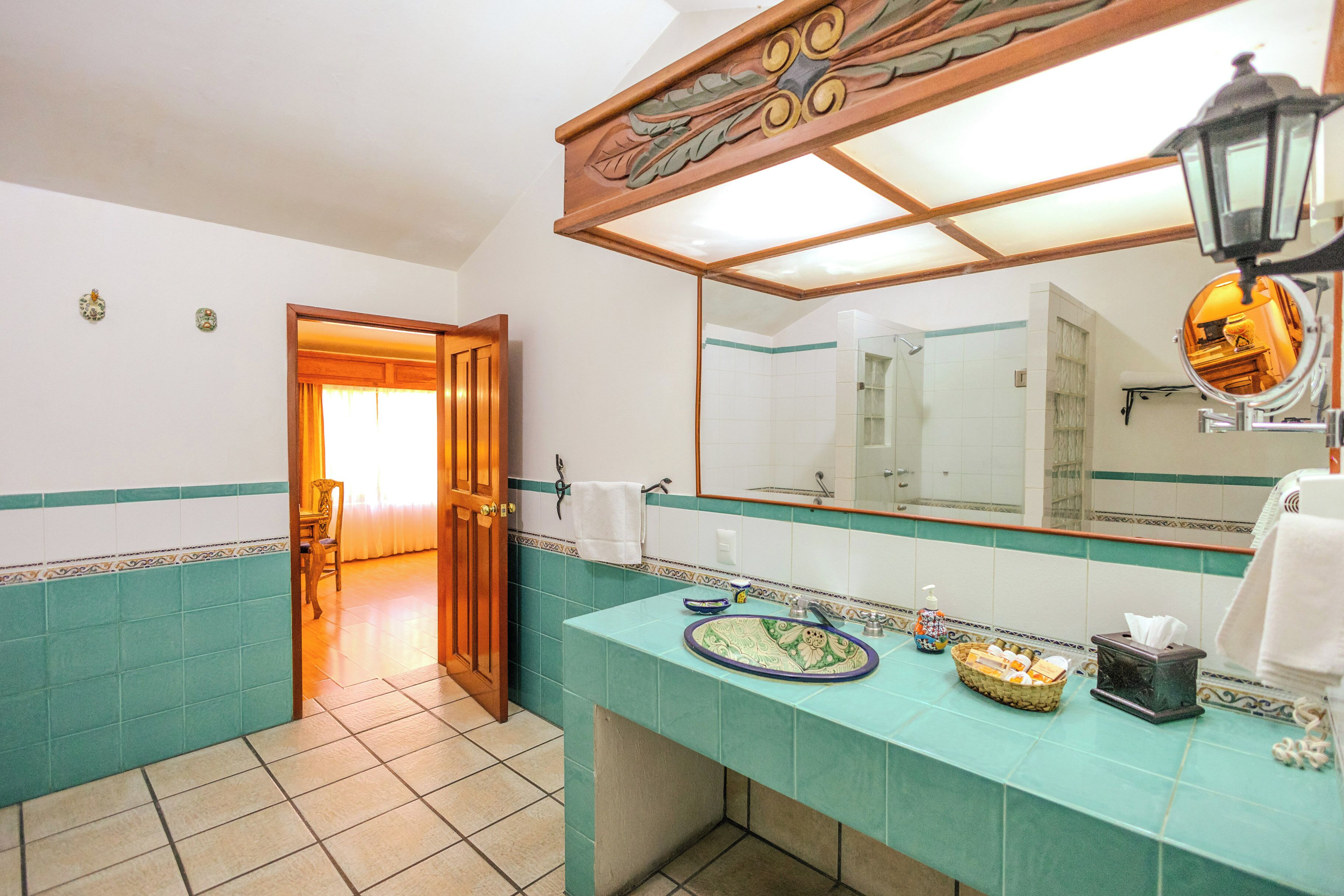 Un baño con un espejo grande, un lavabo con una pileta decorativa, una zona de ducha y una puerta que da a otra habitación.