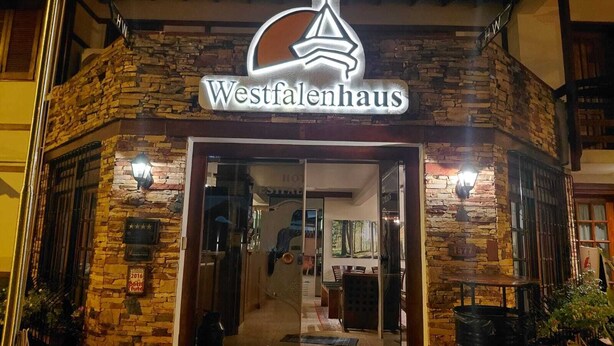 Entrada de un hotel Westfalenhaus con fachada de piedra, puerta de cristal y un letrero en la parte superior.