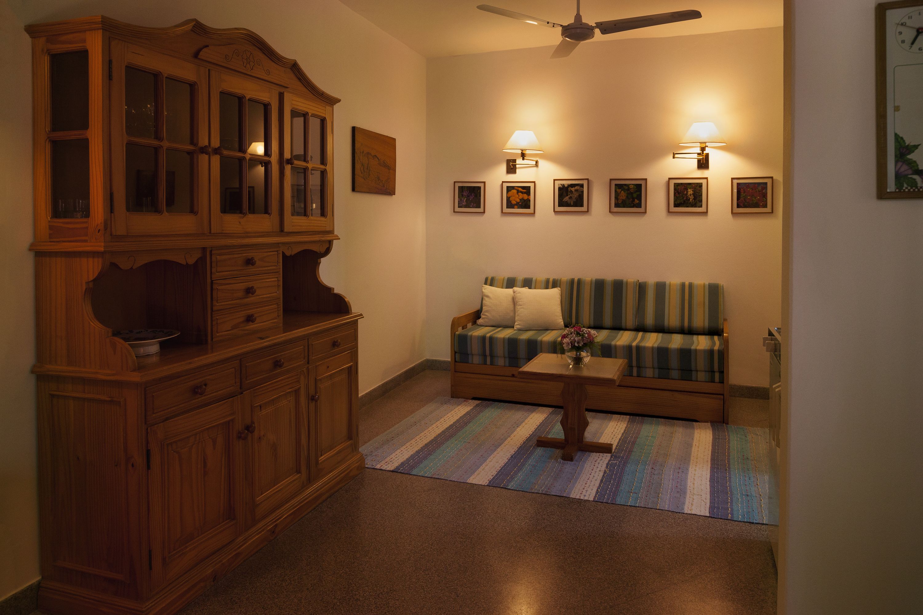A living room with a wooden cabinet, a striped sofa, a coffee table, and wall-mounted lamps.