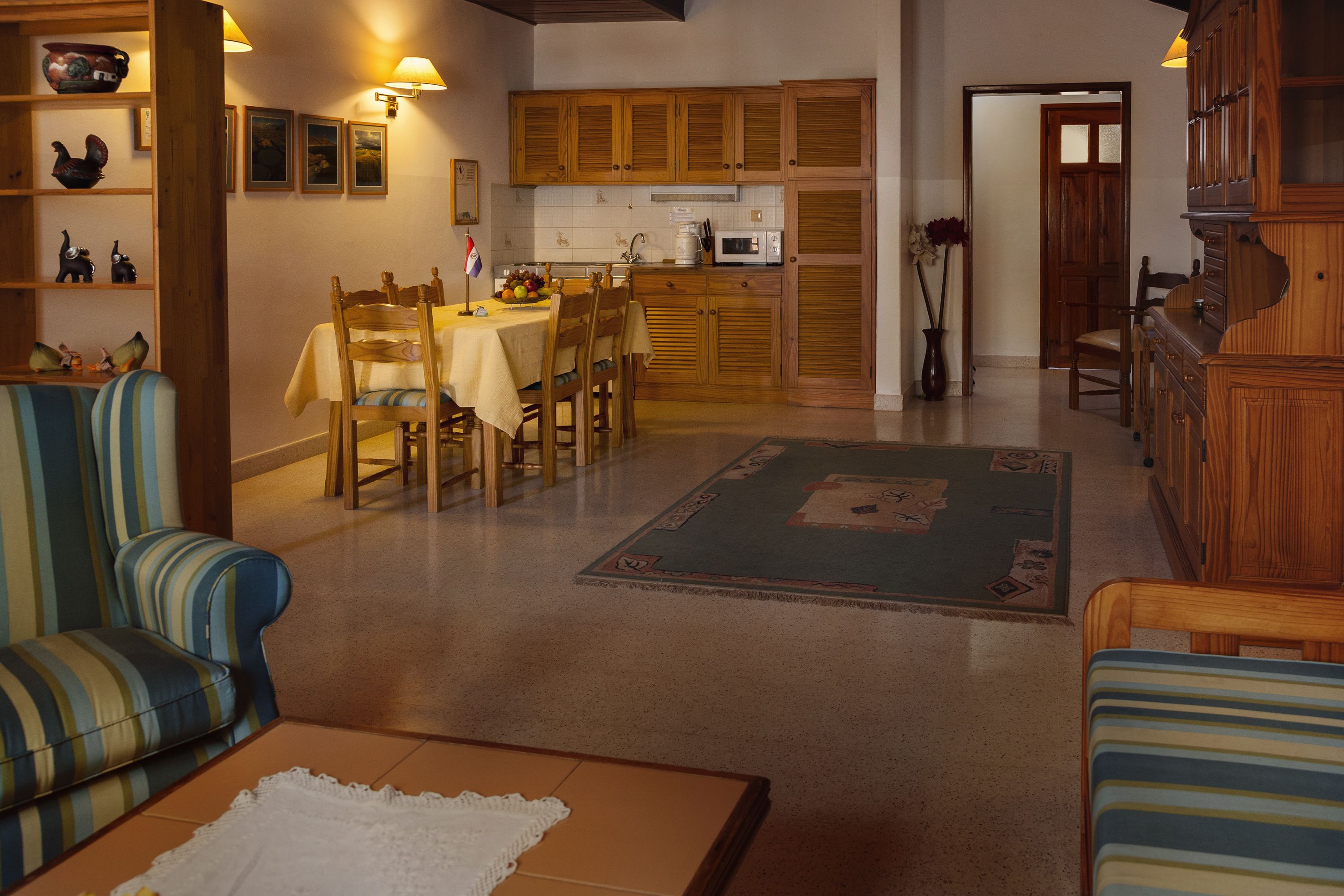A dining area with wooden cabinets, a table set for four, and a kitchen in the background.