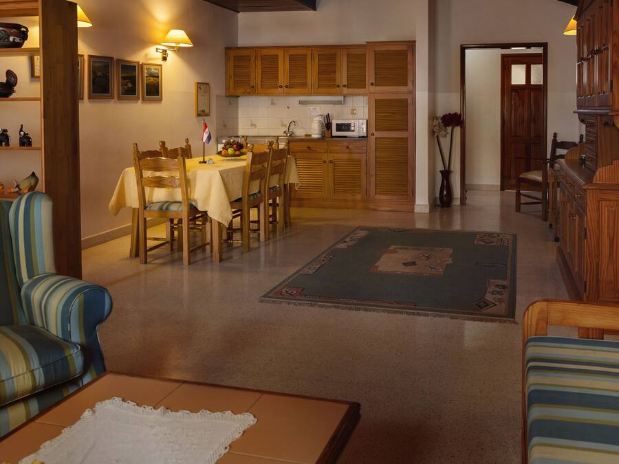 A dining area with wooden cabinets, a table set for four, and a kitchen in the background.