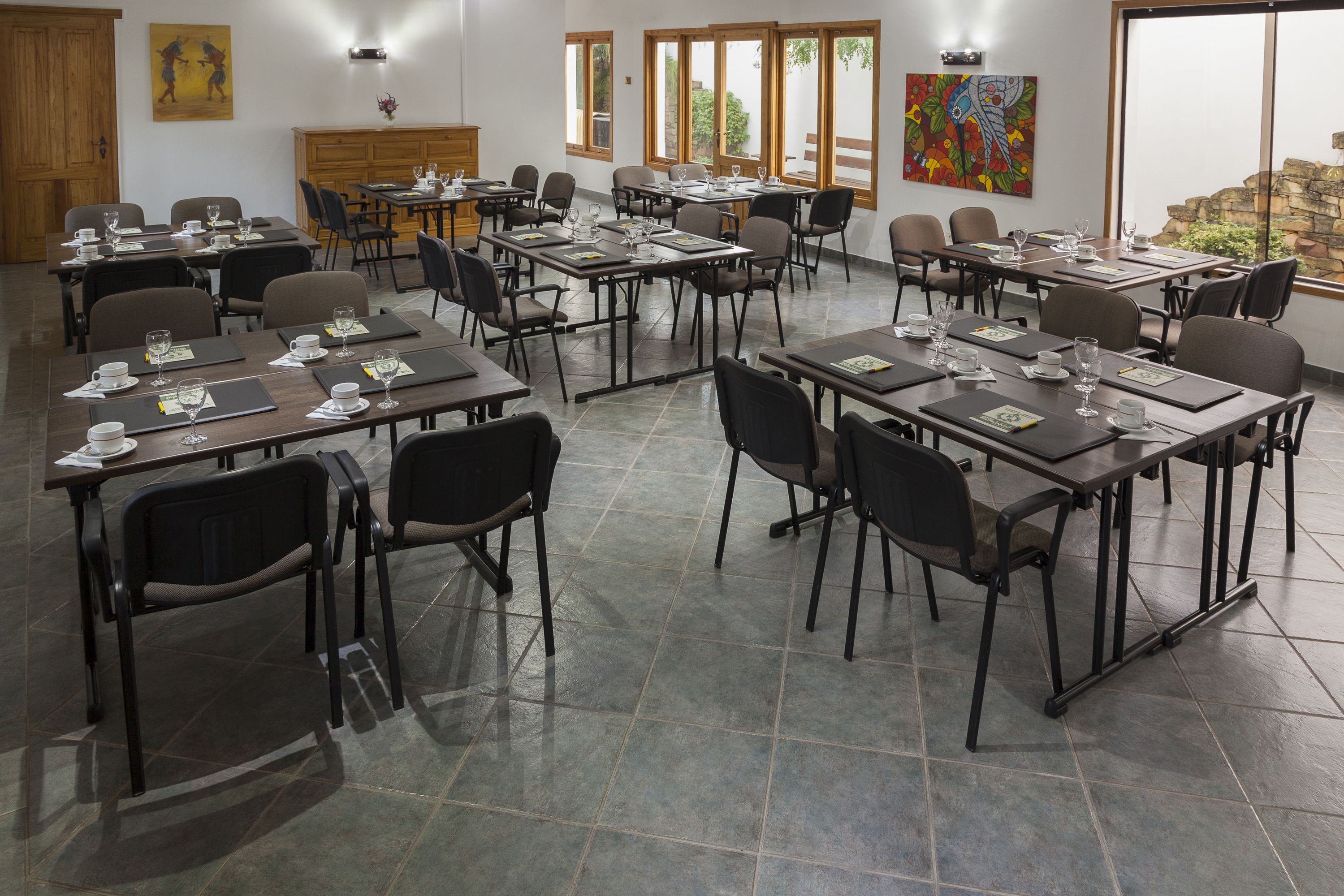 Een congreszaal met meerdere tafels en stoelen, voorzien van naambordjes, glaasjes water en schriften.