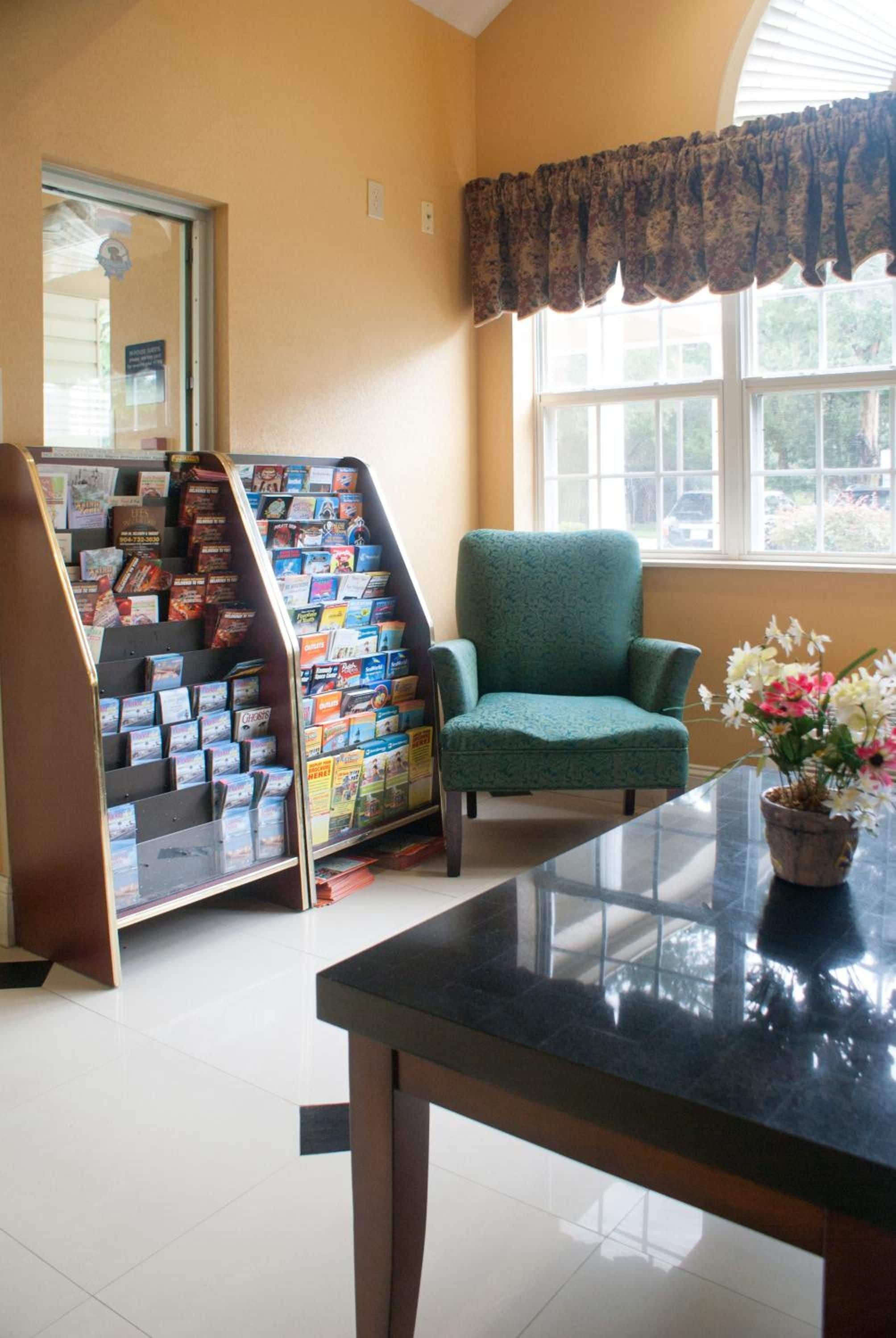 A room with a green armchair, a glass table, a window with a floral curtain, and a display of postcards.