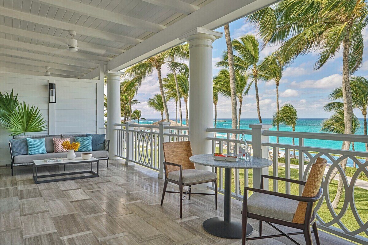 A covered outdoor area with a view of the ocean, furnished with a sofa, chairs, and a table.