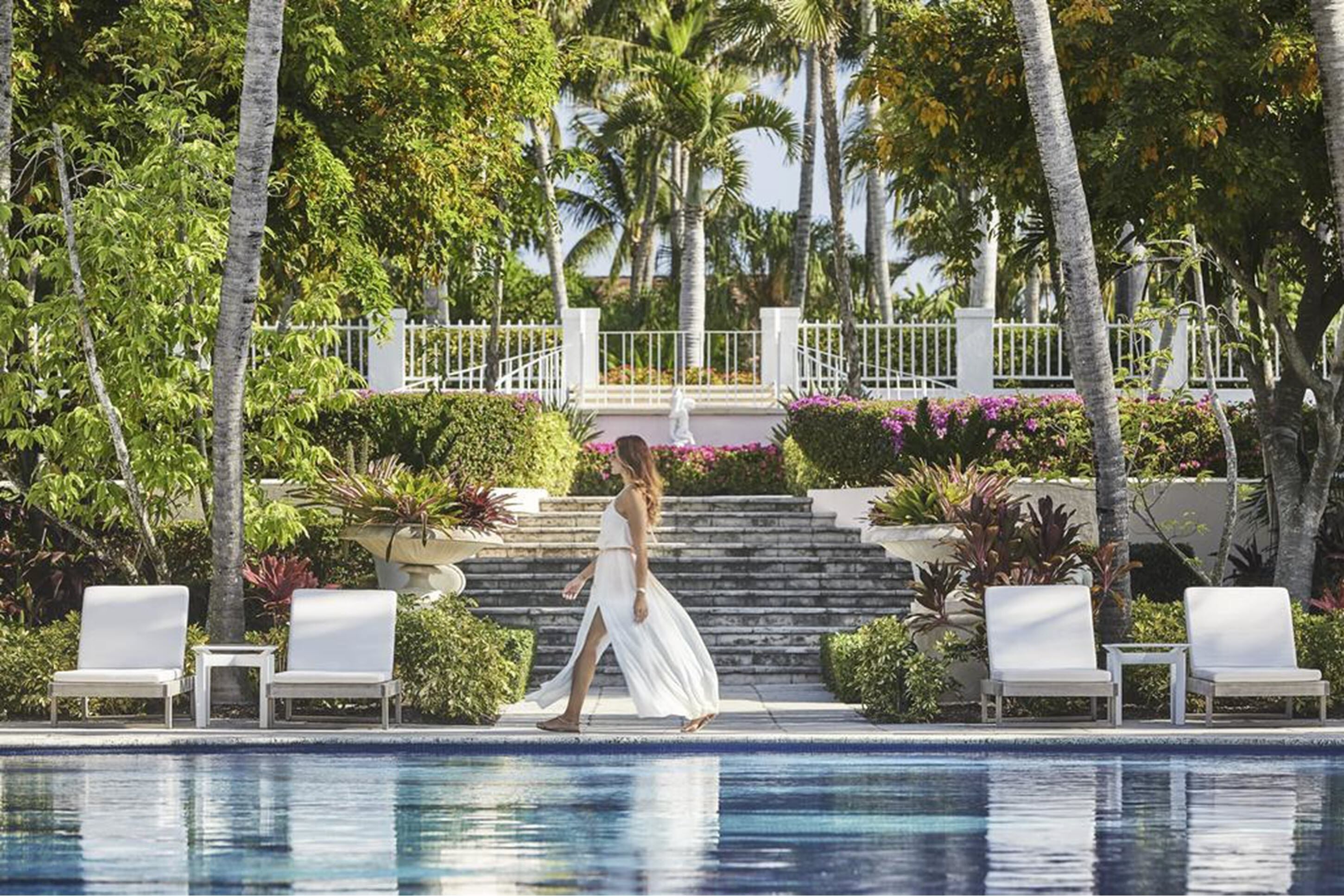 Un área de piscina con sillones de descanso, una escalera y exuberante vegetación tropical.
