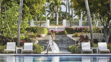 Un área de piscina con sillones de descanso, una escalera y exuberante vegetación tropical.