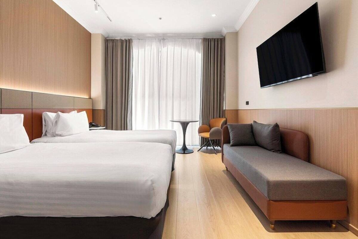 Ein Hotelzimmer mit zwei Betten, einem Sofa, einem Fernseher und einem Fenster mit Vorhängen.