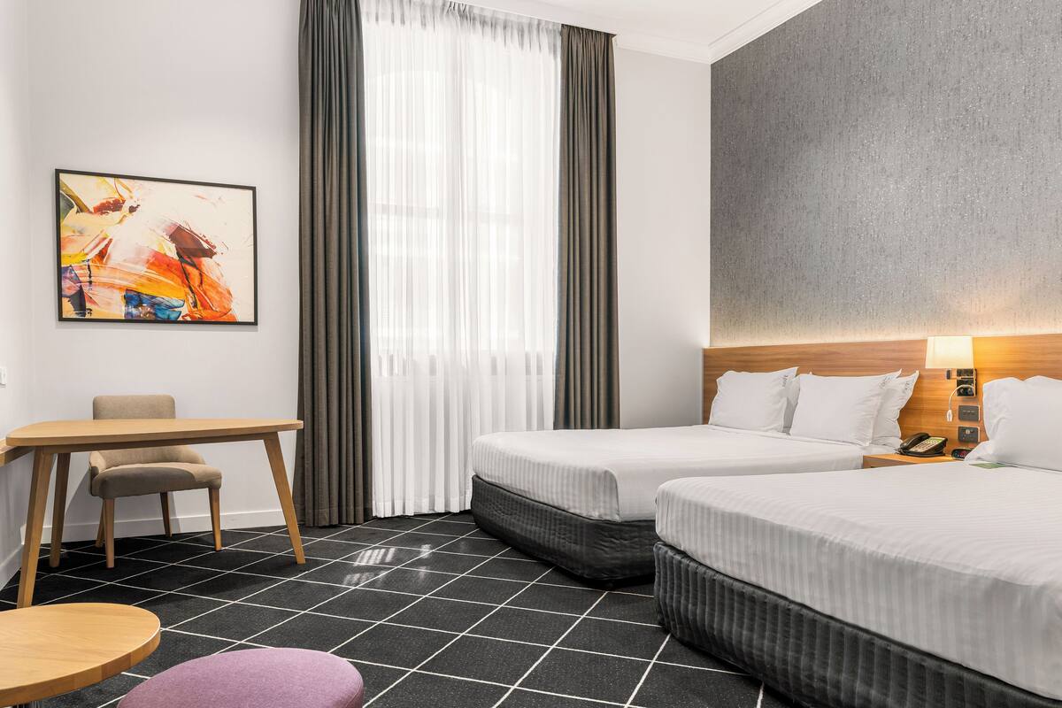 Ein Hotelzimmer mit zwei Betten, einem Schreibtisch, einem Stuhl und einem Bild an der Wand.